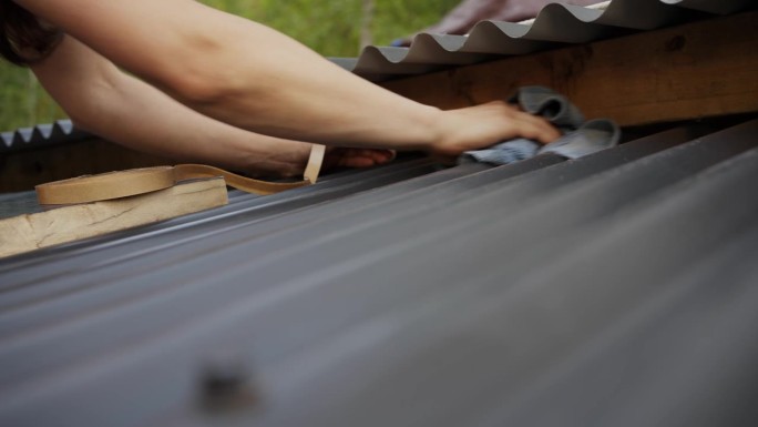 一名妇女正在给甲板上的波纹屋顶板涂胶条