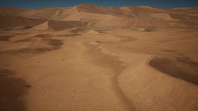 广阔的沙漠地形，金色的沙子映衬着蔚蓝的天空。