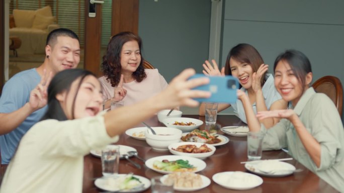 亚洲家庭用手机自拍，坐在家外后院的餐桌旁享受乐趣。多代同堂的家庭一起享受消费。
