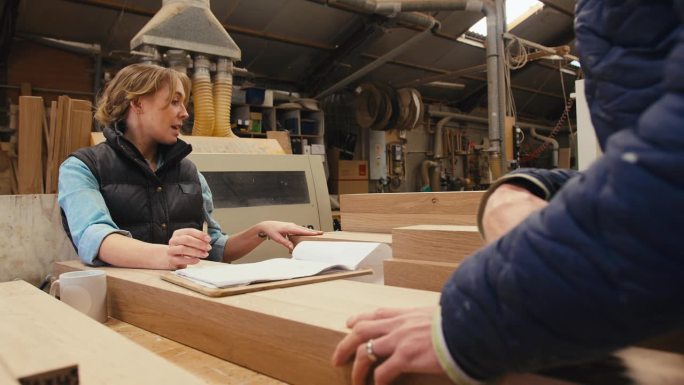 在木工车间工作的男女木匠选择木材和看计划