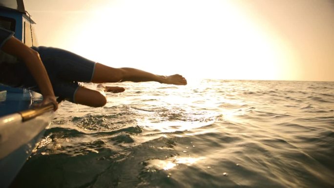快乐的女游泳者爬船在海上对着天空在日落