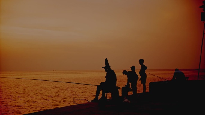 在克罗地亚罗维尼日落时分，一家人在码头上对着橙色的天空捕鱼