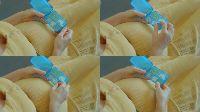 在这段慢动作视频中，一名孕妇坐在沙发上。她从一个塑料盒里取出一粒维生素或食物补充剂。镜头聚焦在她的手
