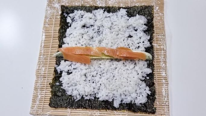 厨师在做寿司时把米饭和三文鱼放在海苔片上