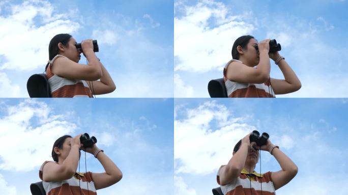 在一个阳光明媚的日子里，年轻女子在山上拿着双筒望远镜。徒步旅行时使用双筒望远镜的妇女。徒步旅行的女人