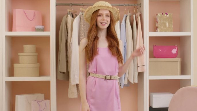 可爱的微笑女性戴着帽子，穿着粉红色的裙子，在镜头前摆姿势，享受着这身打扮