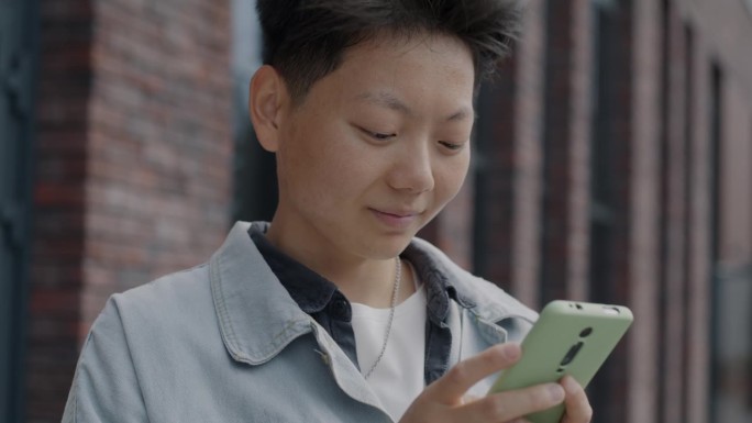 无忧无虑的亚洲学生站在城市街道外，用智能手机触屏享受社交媒体