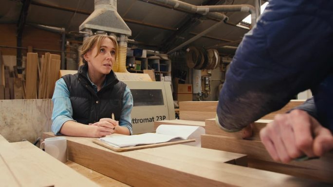 在木工车间工作的男女木匠选择木材和看计划