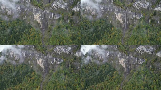 从左到右的航拍照片，一条细细的小溪瀑布从高山顶上流下，周围都是云和雾Klöntalersee瑞士格拉