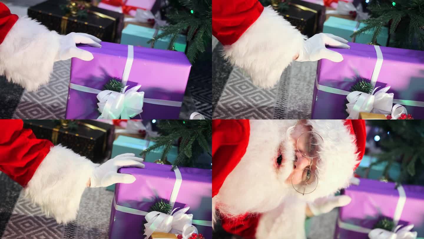 Сlose圣诞老人的手把礼物放在树下，狡猾地看着相机的节日准备