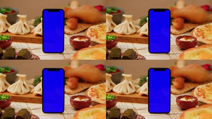 带色度键的手机放在餐桌上，周围是格鲁吉亚菜。阿拉伯的食物。穆斯林菜。khachhapuri, khi