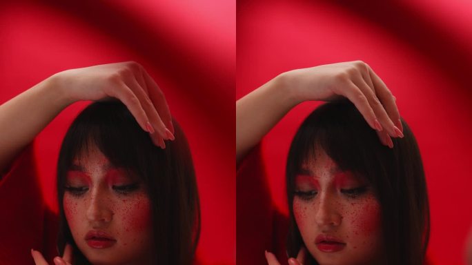 亚洲模特女孩在工作室里把手放在脸旁边，摆姿势拍照。特写红色背景。魔术服装艺伎在行动中的红色。垂直视频