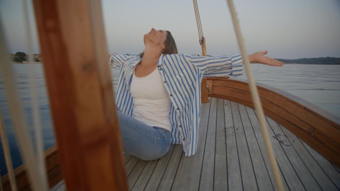 漂浮的宁静:一个女人在帆船的甲板上举起双臂，享受着这一刻