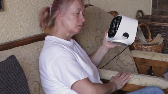 成年妇女坐在沙发上，用家用小风扇、家用电器给自己降温