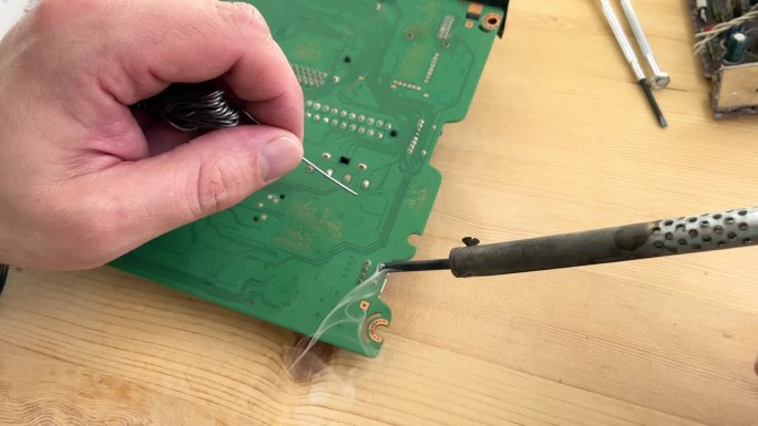 用铁工具在绿色电路板上焊接微芯片处理器。具有电子服务技术和宏观计算机概念背景。
