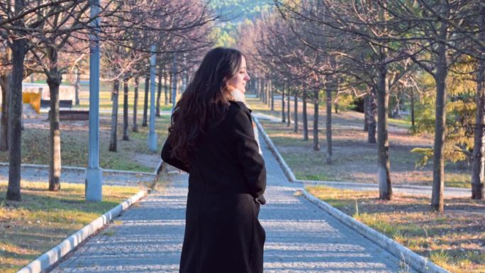 黄昏时分，一名身穿大衣、围着围巾的女子走过一座秋天的公园
