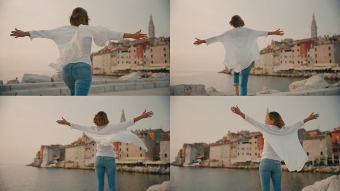 克罗地亚罗维尼的老城区，悠闲的女游客在码头上伸开双臂奔跑的后视图