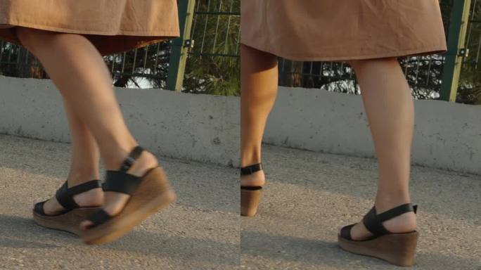 垂直视频。一个女人的腿，她爬上陡峭的路在高跟凉鞋与高平台，不舒服的旅行鞋的概念