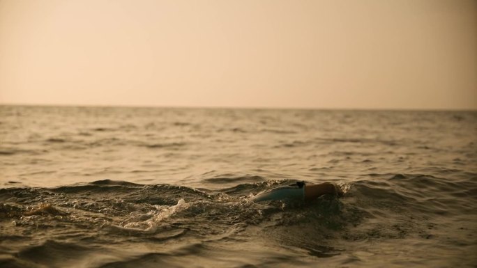手持拍摄的决心女子游泳在海洋对天空在日落