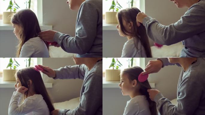 早上，妈妈在房子的窗口用按摩梳梳她心爱的女儿的长发。间隔拍摄。头发护理。