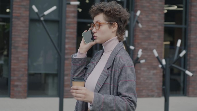 商务女士走在街上，拿着咖啡杯边走边讲手机