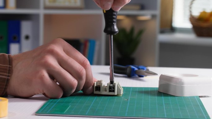 男电工在家里的桌子上修理插座并用螺丝刀拧紧螺栓，特写