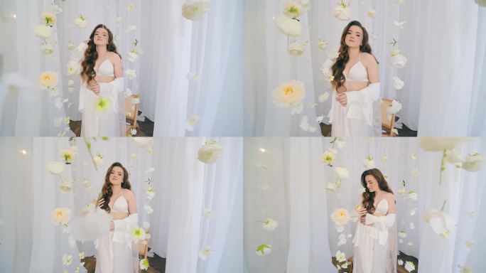 一位美丽的新娘戴着白色的头纱，在白色的窗帘和悬挂的鲜花中为相机摆姿势。一个穿着内衣的模特在镜头前摆姿