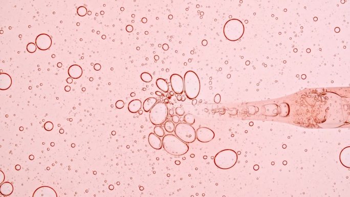 透明的粉红色液体油，血清，凝胶从移液器到培养皿。化学实验室研究。天然有机化妆品，医药。生产天然化妆品