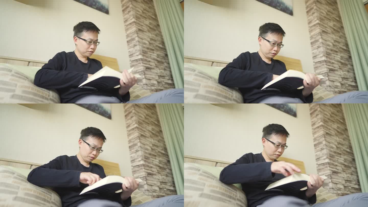 积极的亚洲男人戴着眼镜在家里的床上看书
