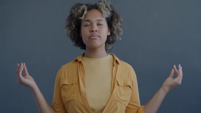 慢动作肖像年轻的非洲裔美国妇女冥想放松集中在灰色背景的压力管理