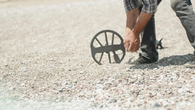 海滩上一个拿着金属探测器的男人正在用手筛选石头。他发现了一些东西。