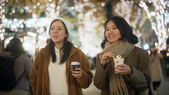 两个亚洲女人在夜晚的城市里散步和聊天，背景是许多圣诞灯。