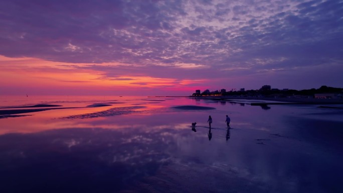 在紫色的夕阳下，一对夫妇在沙滩上遛狗