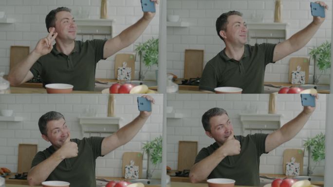 快乐的男子在厨房用智能手机自拍，竖起大拇指
