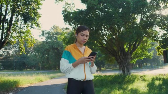 亚洲体育女性使用智能手机和在公园散步。