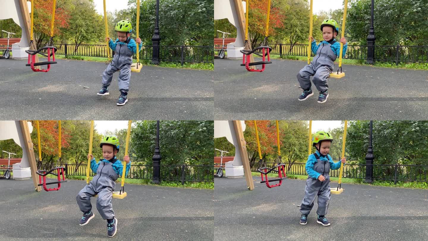 初学走路的孩子戴着安全帽在秋天公园的儿童游乐场荡秋千