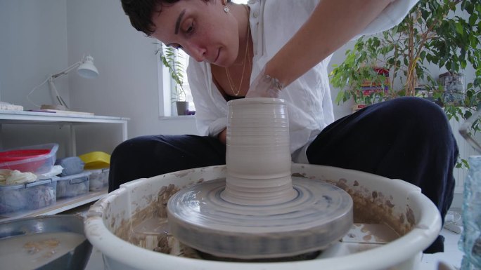 制作优雅与美丽:一位年轻的陶瓷艺术家熟练地在陶轮上塑造了一个粘土花瓶，展示了创造力，工艺，自我表达的