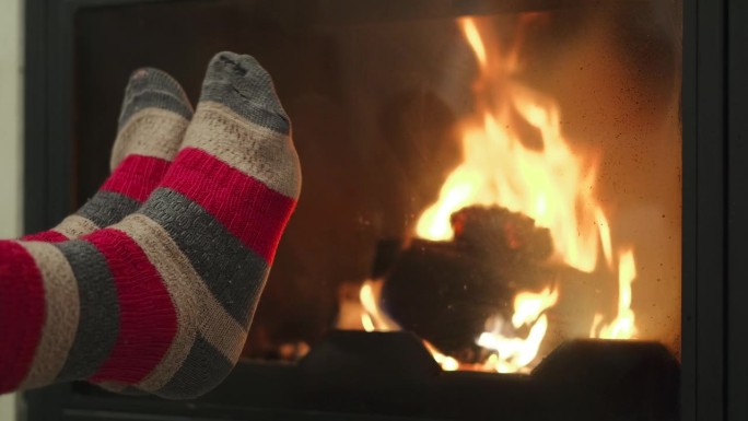 在秋天的森林里徒步旅行后，一位妇女穿着旧袜子在壁炉旁温暖她疲惫的脚，这是徒步旅行后的放松