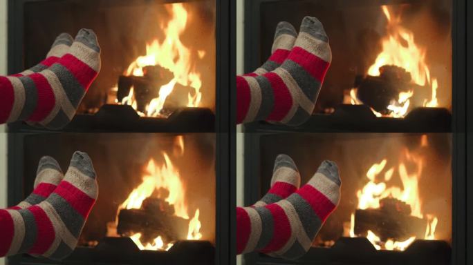 在秋天的森林里徒步旅行后，一位妇女穿着旧袜子在壁炉旁温暖她疲惫的脚，这是徒步旅行后的放松