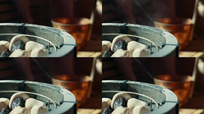 将水洒在桑拿炉的热桑拿石上，用勺子或长柄勺从一个被称为kip或桶的水桶里取水。炉子在前景，小床和人在