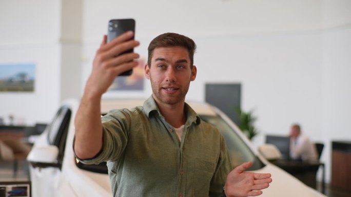 汽车经销商在网上发布了一幅快乐的男视频博主的中景照片，他正在评论新款自动驾驶智能手机。友好男子视频的