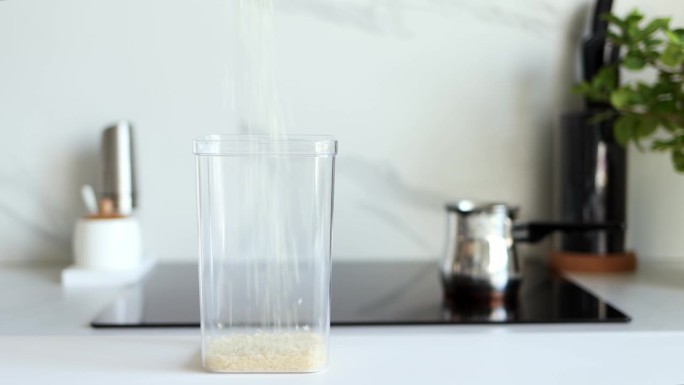 白色的生米倒入一个透明的容器中，以现代厨房为背景。健康食品和营养理念。安全、生态、健康产品。生态包装
