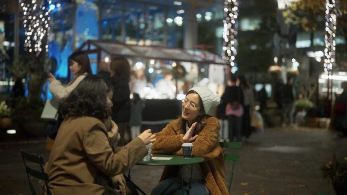 快乐的亚洲朋友聊天，喝热饮在街边的咖啡桌在城市的夜晚