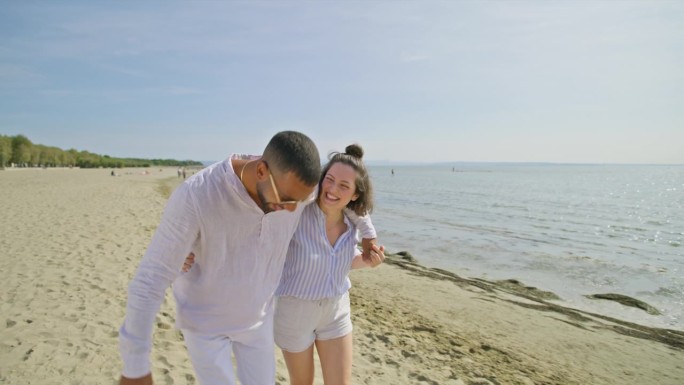 一对年轻的夫妇在阳光明媚的日子里微笑着走在沙滩上