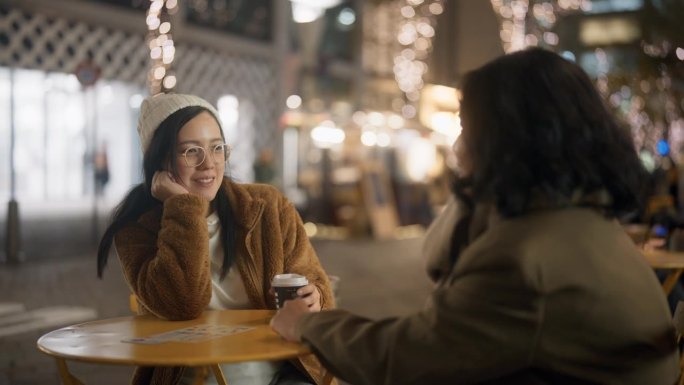 一群亚洲朋友坐在圣诞市场上，一边喝着热咖啡，一边取暖。