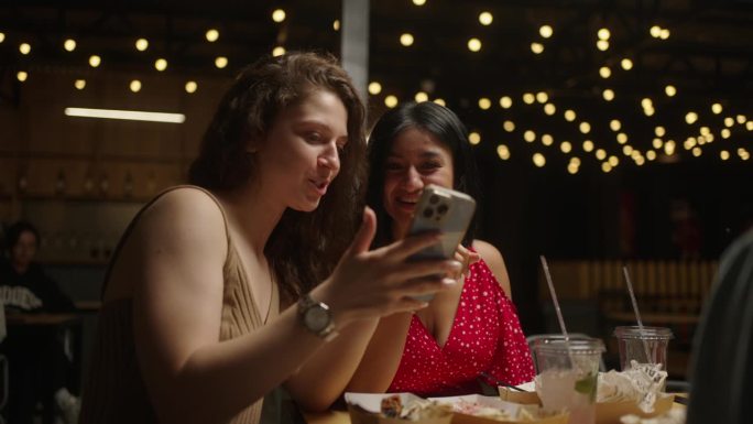 多民族女性朋友在智能手机上看照片，在餐厅吃饭