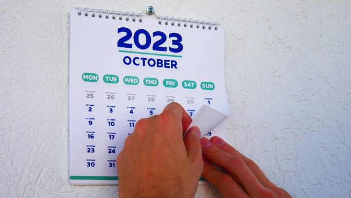 两个男人的手撕掉了墙上的日历，10月2023页，紧接着是下一个标有黑色星期五日期的日历