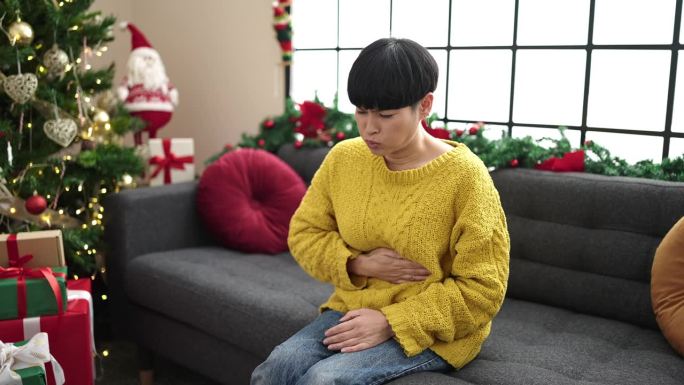 胃痛的中国年轻女子坐在家里的圣诞树旁