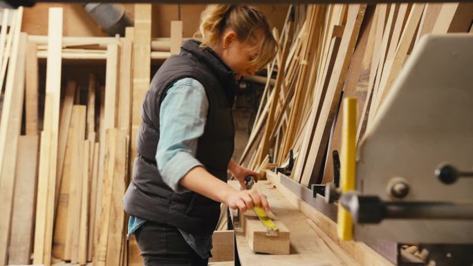 木工车间女木匠用伸缩钢尺测量木材