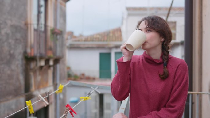 意大利卡塔尼亚，一名女子站在阳台上喝着清晨的咖啡